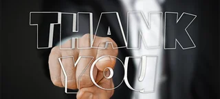A finger points towards the viewer; in the foreground, the words "Thank You" are written in large 3D letters against a blurred business background.